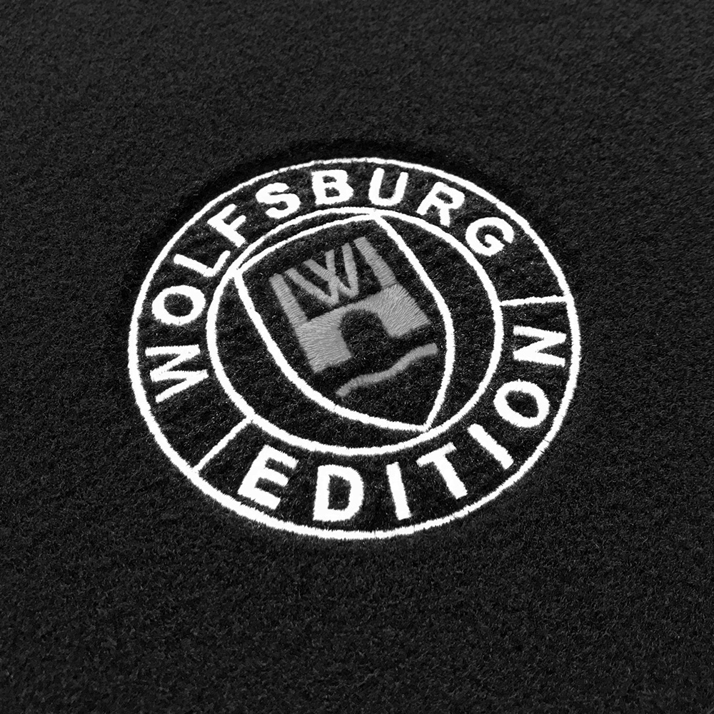 Das gestickte Wolfsburg Editions Logo auf einem schwarzen Teppich und das Logo ist in grau.