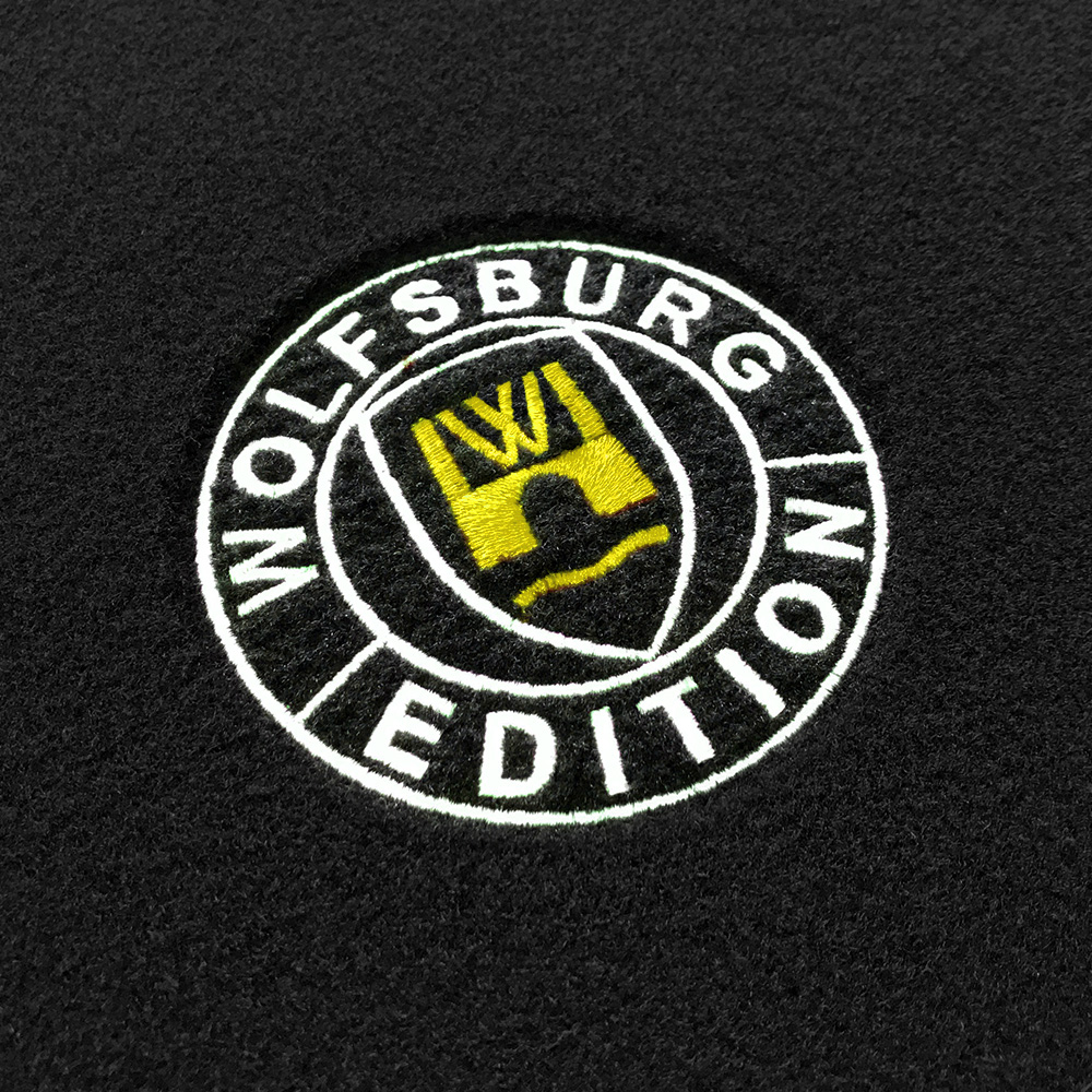 Das gestickte Wolfsburg Editions Logo auf einem schwarzen Teppich und das Logo ist in gelb.